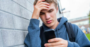 A teenage boy upset looking at his smartphone.